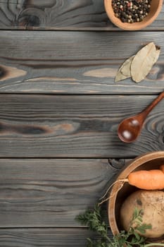 Flavorings and vegetables in tableware. Layout of foodstuffs on wooden table. Planking, place for text, flat lay. Greens, bay leaf, potato, peppercorns and carrot. Prepare ingredients for cooking.