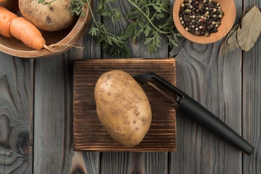 Peeling yellow potato with vegetable peeler. Flat lay view. Fresh raw unpeeled potato. Cutting peel on kitchen wooden board. Prepare ingredients for cooking. Healthy food. Vegetables and flavorings.