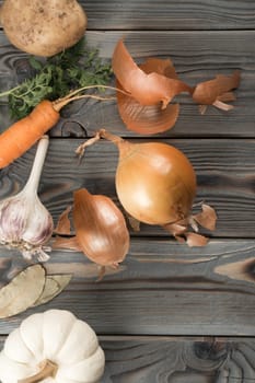 Peeling spicy white onion. Flat lay view. Fresh raw vegetables and flavorings. Skinning, rinding onion on kitchen wooden table. Prepare ingredients for cooking. Healthy diet, food waste.