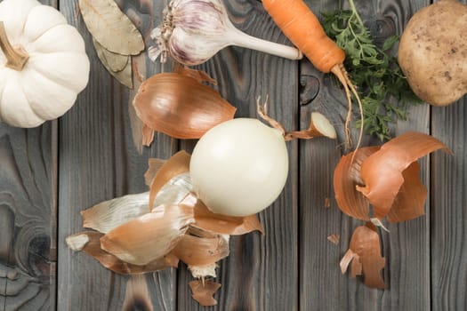 Peeling spicy white onion. Flat lay view. Fresh raw vegetables and flavorings. Skinning, rinding onion on kitchen wooden table. Prepare ingredients for cooking. Healthy diet, food waste.
