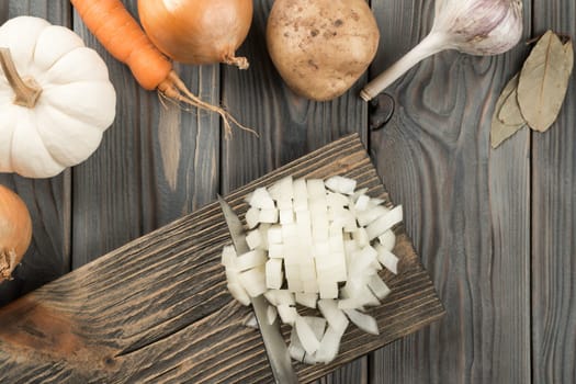 Cutting spicy onion with knife into cubes on kitchen wooden board. White diced onion. Flat lay view. Layout of fresh raw vegetables. Prepare ingredients for cooking. Healthy diet, foodstuffs.