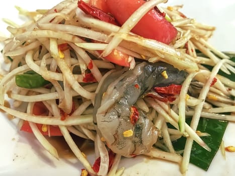 Papaya salad with fresh shrimp in a white plate, it is the staple food of Thai people.