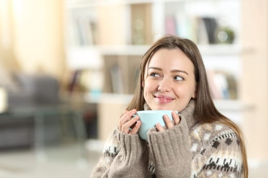 Happy teen drinking coffee and dreaming at home in winter looking at side