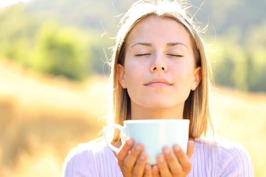 Front view portrait of a woman smelling coffee cup outdoors