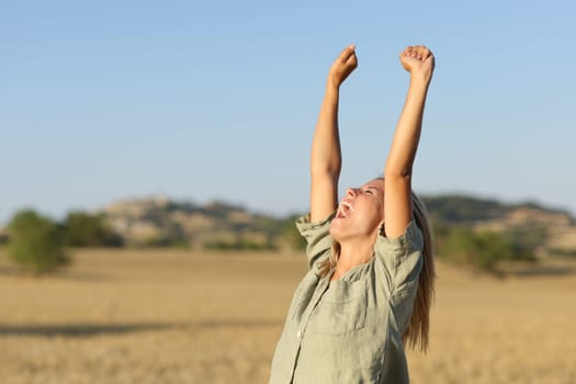Teen raising arms in a golden wheat field at sunset