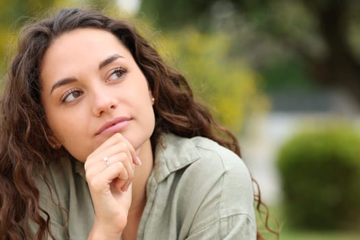 Front view portrait of a pensive woman looking at side in a park