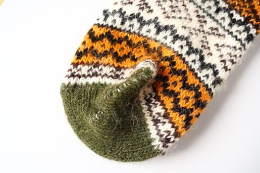 Fragment of an ornament on a knitted woolen sock. Winter motives. Beige, brown, white, green, black threads for hand knitting pattern. Knitted front heel with hand-knitted seam. White background