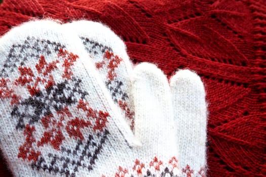 Fluffy white knitted mohair mittens with a traditional floral pattern on the back. A pair of mittens fashion accessories. Knitted with red and black threads geometric jacquard pattern. Winter clothes