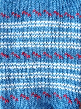 A fragment of an ornament on a knitted woolen sweater, mitten or sock. Winter motives. Blue, brown, red threads for hand knitting. Knitted pattern. Dashes, lines and stripes