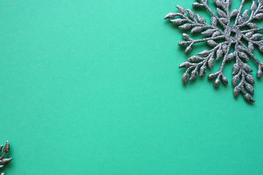 New Year or Christmas background with decorative snowflake around the edges of a sheet of colored paper. Copy space. Blue silver snowflake on a green background. Postcard, background or invitation.