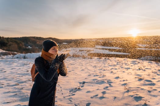 A woman blows snow from her palms on a sunny winter evening.