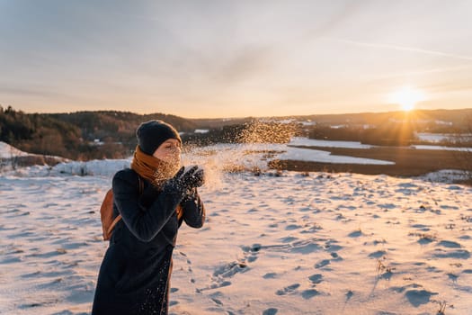 A woman blows snow from her palms on a snow-covered field in winter.