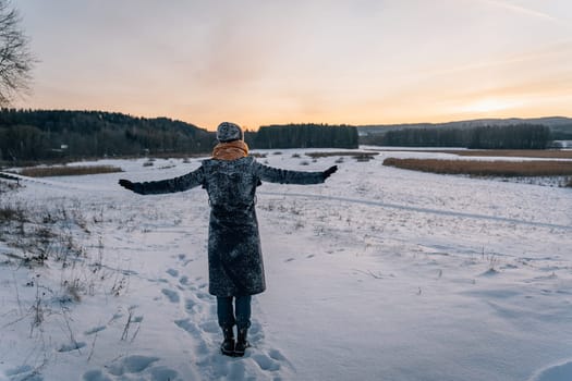 View of a woman in a coat and hat covered in snow with her hands spread out in torn.