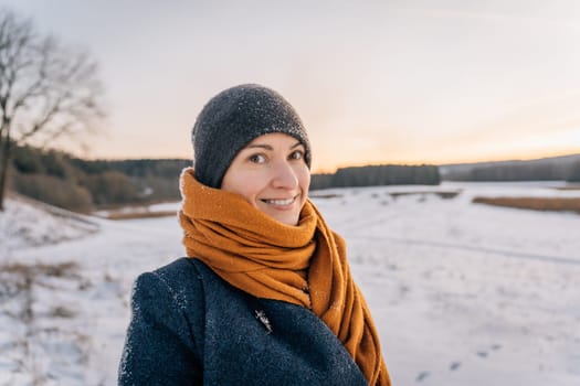 Portrait of a young woman in winter clothes and a hat wrapped in a scarf with a big smile.