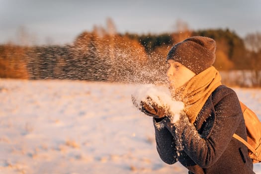 A woman blows a handful of snow from her hands at sunset in the evening.