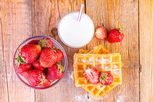 homemade waffles with strawberries and glass with milk on wooden background