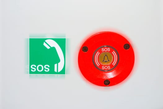 An emergency switch and an SOS sign sticker with a telephone handset on the wall of a disabled toilet.
