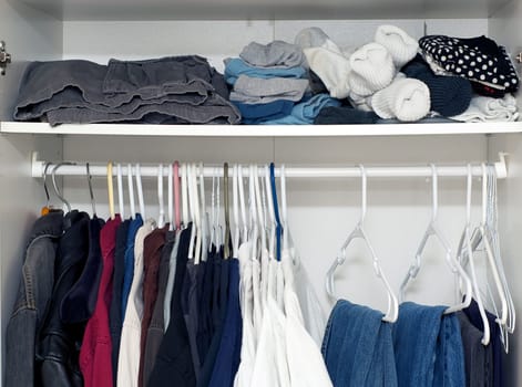 Looking inside a man's closet or armoire full of clothes hanging on hangers and laying on shelf.
