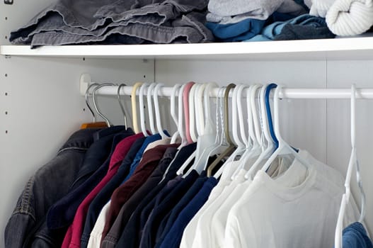 Looking inside a man's closet or armoire full of clothes hanging on hangers.
