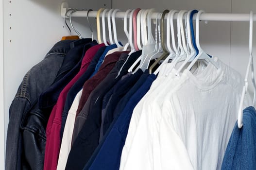 Looking inside a man's closet or armoire full of clothes hanging on hangers.