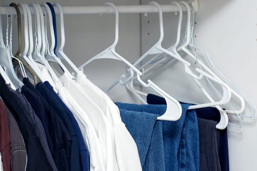 Looking inside a man's closet or armoire full of clothes hanging on hangers.
