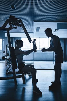 Fit female exercising in gym with help of her trainer