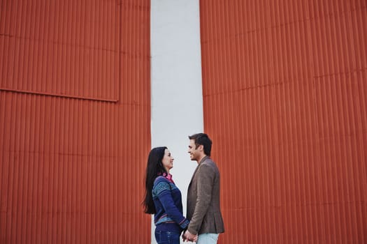 Young couple in casualwear looking at one another by wall
