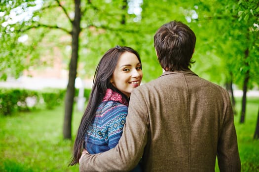 Back view of young man embracing his girlfriend outdoors