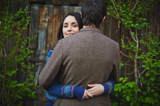 Young woman embracing man and looking at camera out of his shoulder