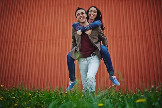 Young man holding happy woman on his back outdoors