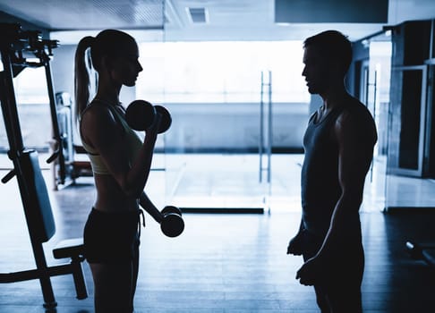 Young woman doing exercise with dumbbells with her trainer near by