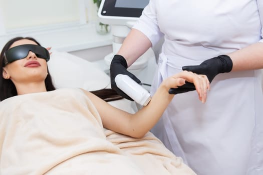 The process of laser hair removal of the female body. professional cosmetology, epilation of the hand zone. Girl in goggles. Body care concept