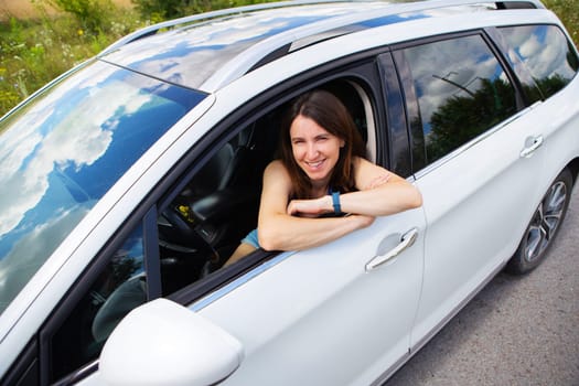 Young girl driving a car, the girl looks in the side mirror and smiles. Delivery for the right to drive a car