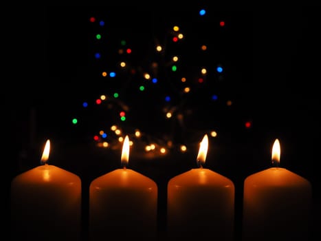 Four Advent candles burning with a colorful Christmas lights background, space for your text