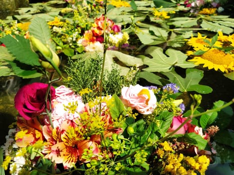 Yellow decorative sunflowers, pink and red roses in a bouquet floating in the water of a fountain. Plucked buds as decoration for a summer holiday. Ivan Kupala, summer solstice. Harvest festival