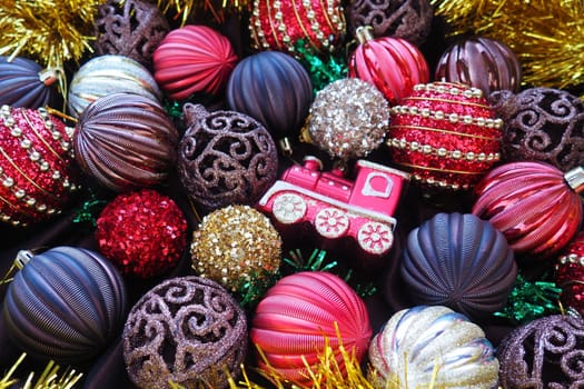 Christmas background with yellow tinsel and Christmas balls. Beautiful Christmas toys and decorations. Red, gold, brown, silver, yellow striped shiny balls. Toy festive train locomotive