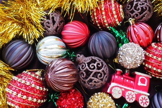 Christmas background with yellow tinsel and Christmas balls. Beautiful Christmas toys and decorations. Red, gold, brown, silver, yellow striped shiny balls. Toy festive train locomotive