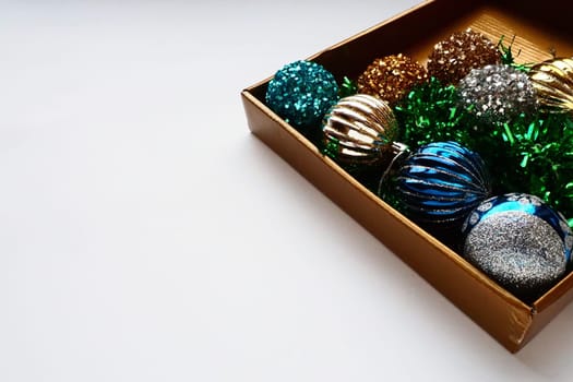 trendy Christmas decorations, colorful balls and tinsel in the lid of a gift box. Shiny beige or brown box for gifts or storage. New Year's Christmas card. Copy space. White background.
