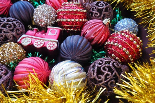 Christmas background with yellow tinsel and Christmas balls. Beautiful Christmas toys and decorations. Red, gold, brown, silver, yellow striped shiny balls. Toy festive train locomotive