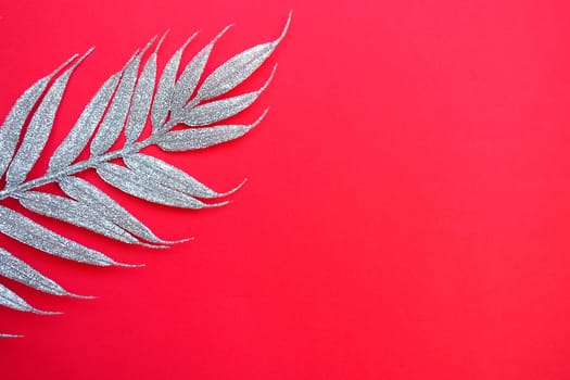 Artificial festive exotic silver branch with long leaves on a bright pink or red background. Copy space. Flat lay. Free space for text. New Year, Christmas, mother's day, birthday background