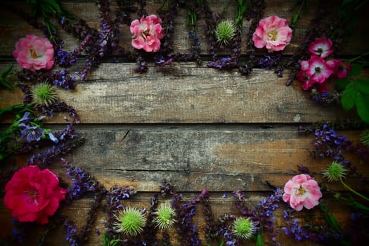 Flowers in a circle on a wooden background. Postcard for the holiday. Roses, geraniums, lavender, sage and hairy chestnuts are placed along the edges on dark boards. Background copy space, flat lay