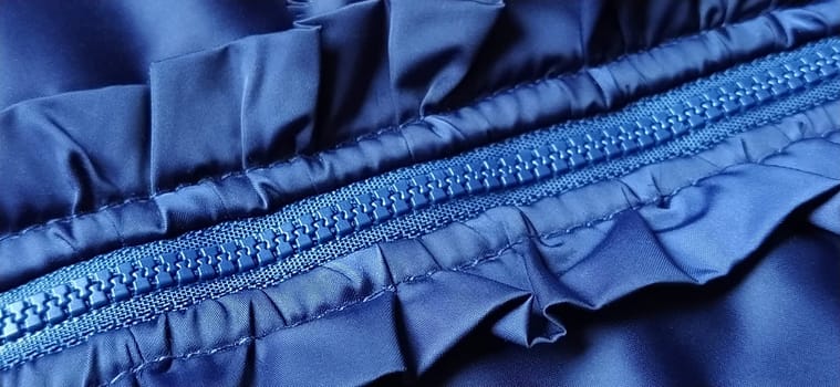 Buttoned zip on a blue raincoat. Waves and folds in the fabric. Beautiful flounces, ruffles, frills. Decorative finishing of a garment. Smocked, sewn silk fabric. Nice casual wear