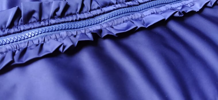 Buttoned zip on a blue raincoat. Waves and folds in the fabric. Beautiful flounces, ruffles, frills. Decorative finishing of a garment. Smocked, sewn silk fabric. Nice casual wear