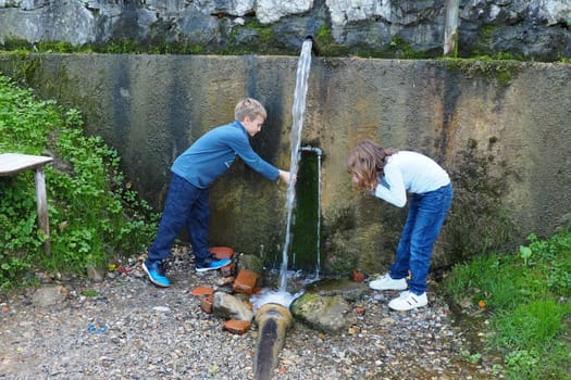 Banja Koviljaca, Loznica, Serbia Mount Guchevo park and forest. Source of mineral sulfuric and ferruginous water Ilidja Chesma Cesma. A jet of water pours out of a tap in a concrete wall. Boy and girl