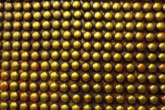 Pimples or spikes made of black and gold metal. Metal large rounded bulges are located geometrically. Unusual industrial abstract chain mail background