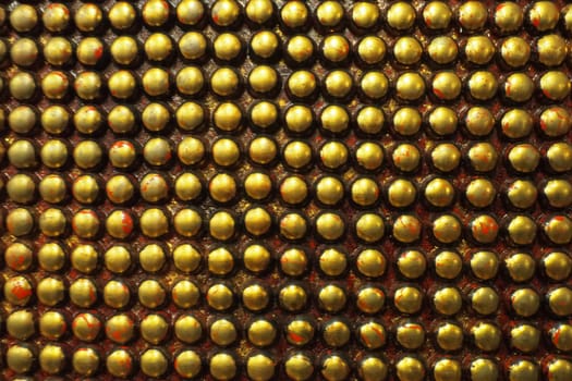 Pimples or spikes made of black and gold metal. Metal large rounded bulges are located geometrically. Unusual industrial abstract chain mail background