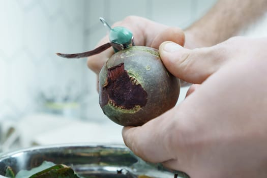 Close-up of unrecognizable man wearing peeling beet with peeler knife over metal bowl full of peelings, standing in kitchen. Recycling, composting, fertilizing, zero waste, organic waste management.