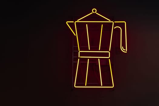 Yellow neon signage in the form of a Moka coffee maker against a black wall