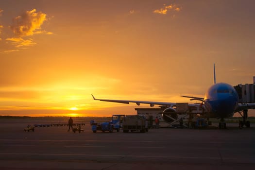 Airport ground crew loading cargo and luggage on a commercial aircraft at dawn.