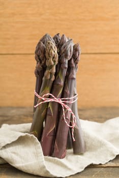 Bunch of violet asparagus on wooden table with linen cloth